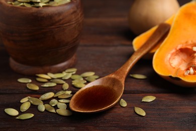 Photo of Spoon with oil and pumpkin seeds on wooden table