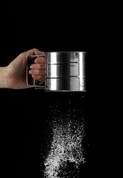 Woman sieving flour against black background, closeup. Space for text