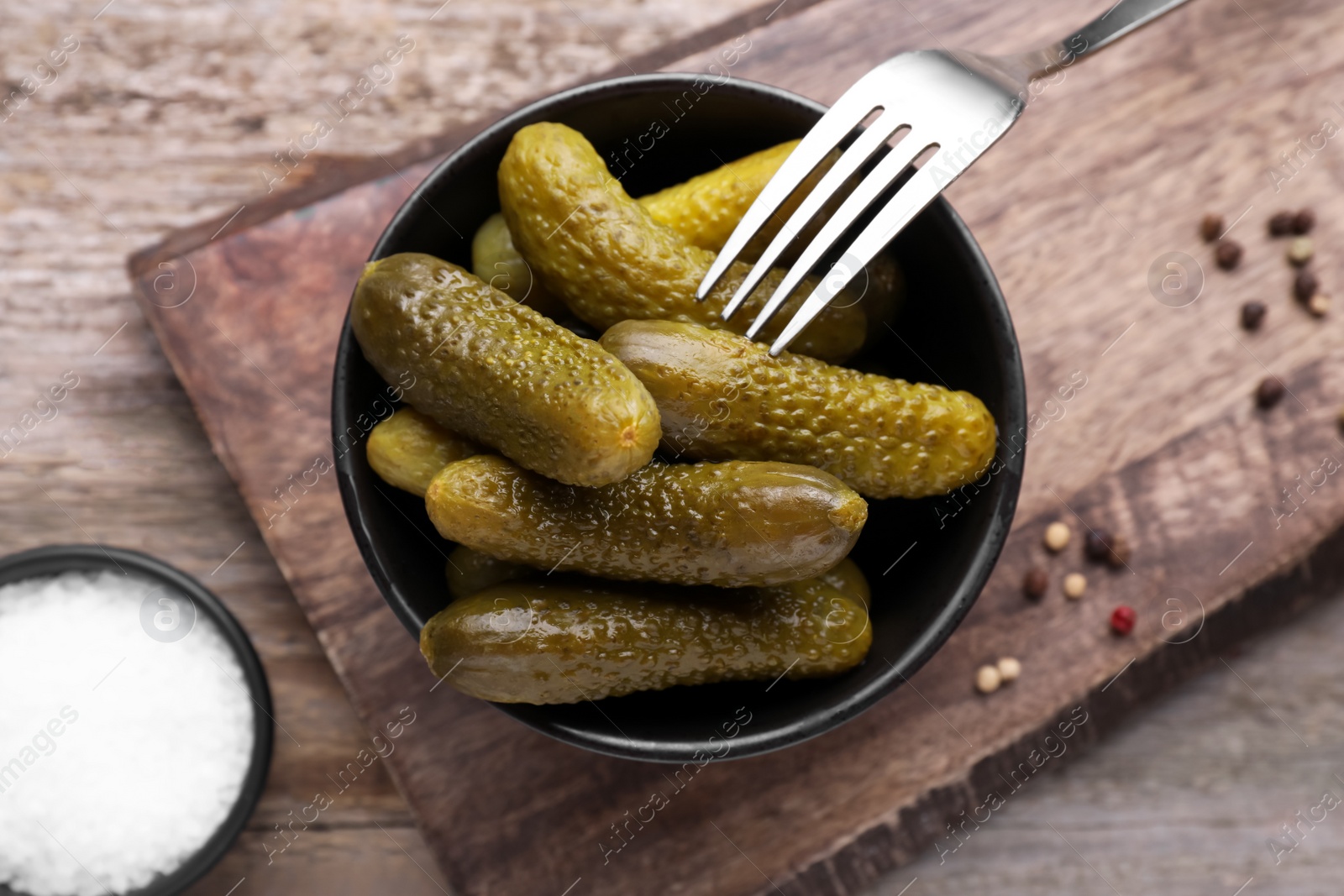 Photo of Bowl with pickled cucumbers and salt on wooden table, flat lay