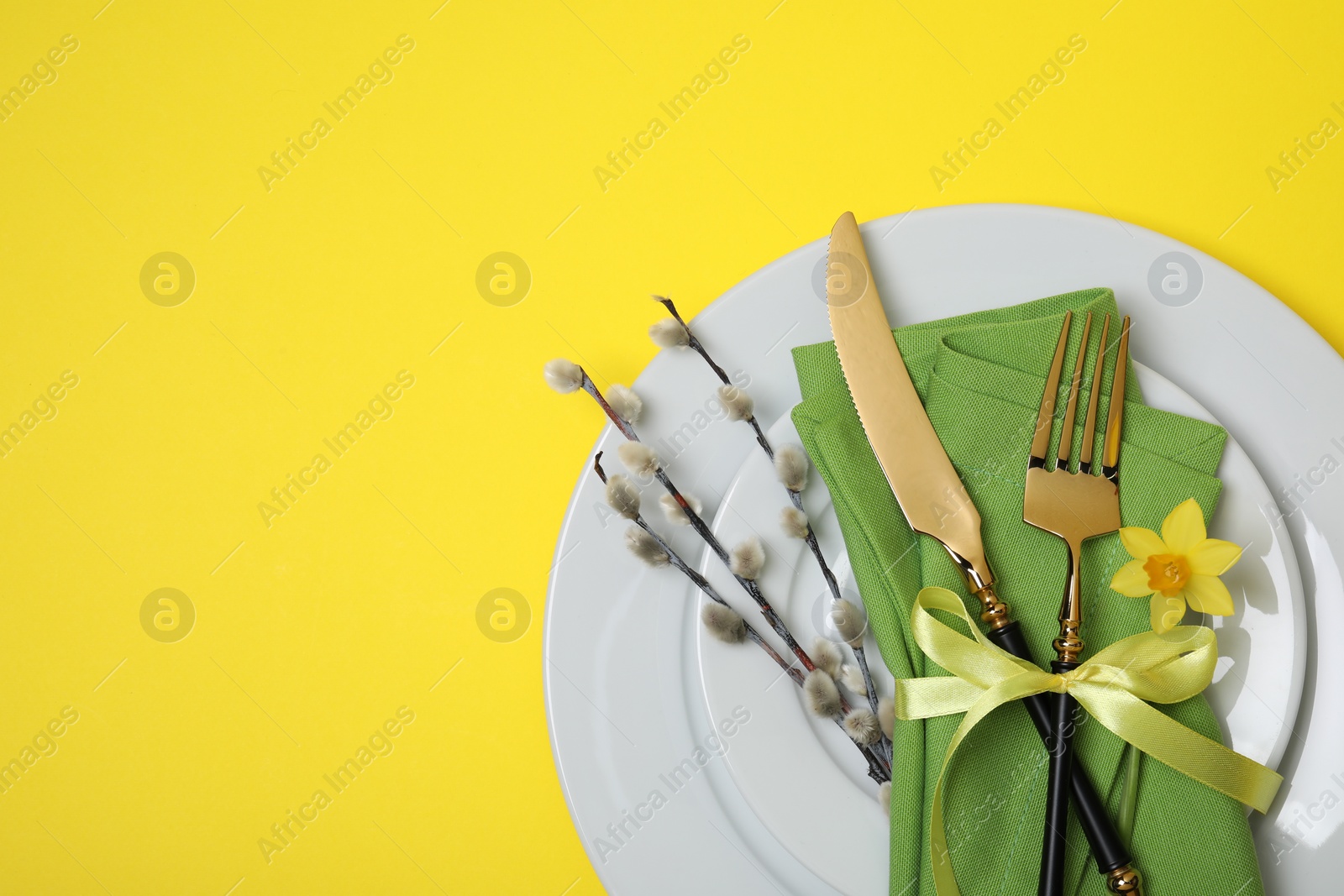 Photo of Festive table setting with willow twigs and space for text on yellow background, top view. Easter celebration