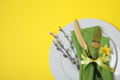 Festive table setting with willow twigs and space for text on yellow background, top view. Easter celebration