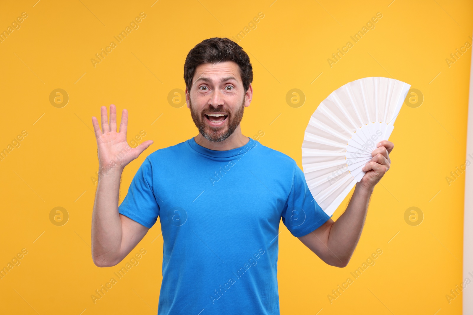 Photo of Emotional man holding hand fan on orange background