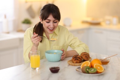 Smiling woman eating tasty cornflakes at breakfast indoors