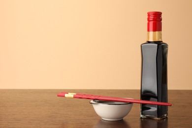 Photo of Bottle, bowl with soy sauce and chopsticks on wooden table against beige background. Space for text