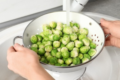 Photo of Woman washing fresh Brussels sprouts in colander, closeup