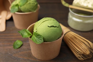 Paper cups with tasty matcha ice cream and bamboo whisk on wooden table, closeup
