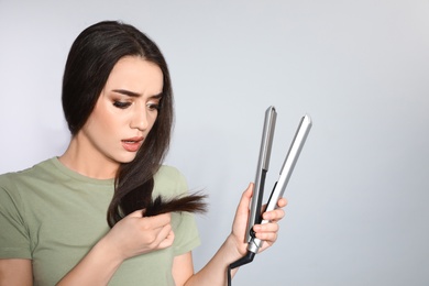 Emotional woman with hair iron on grey background. Space for text