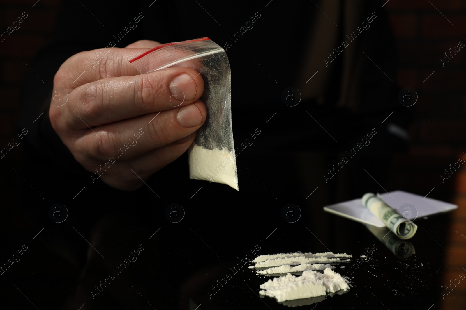 Photo of Drug addiction. Man with cocaine and rolled dollar banknote at black table, closeup