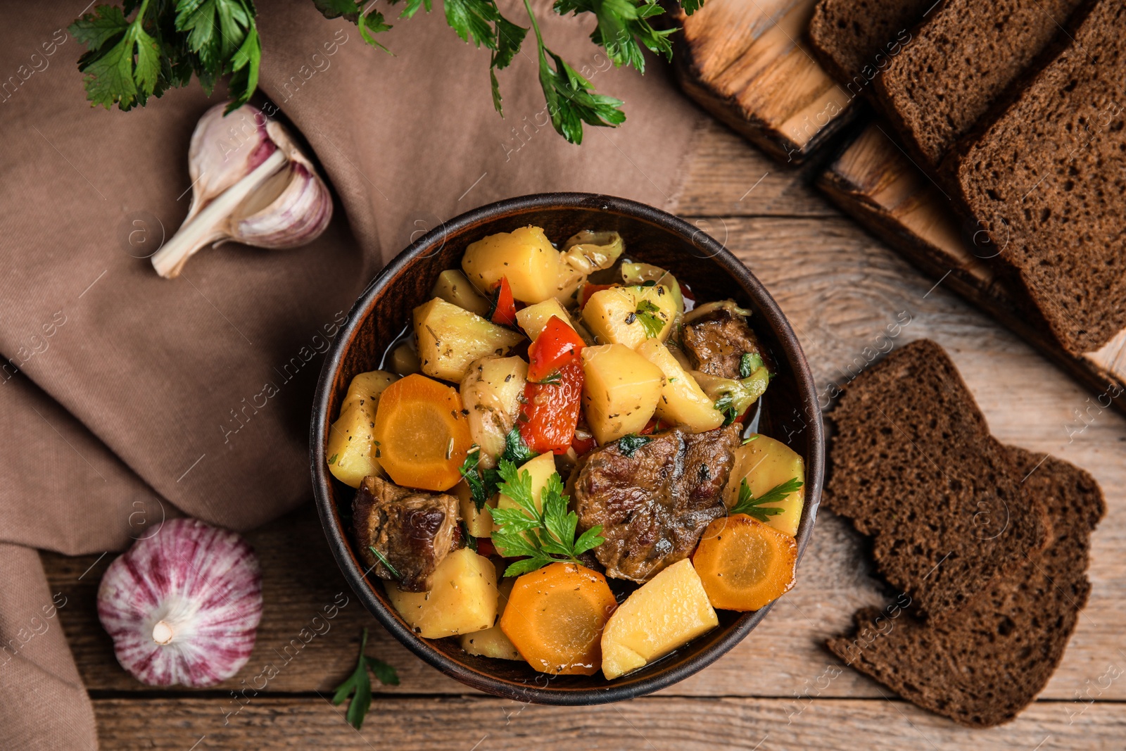 Photo of Tasty cooked dish with potatoes in earthenware served on wooden table, flat lay