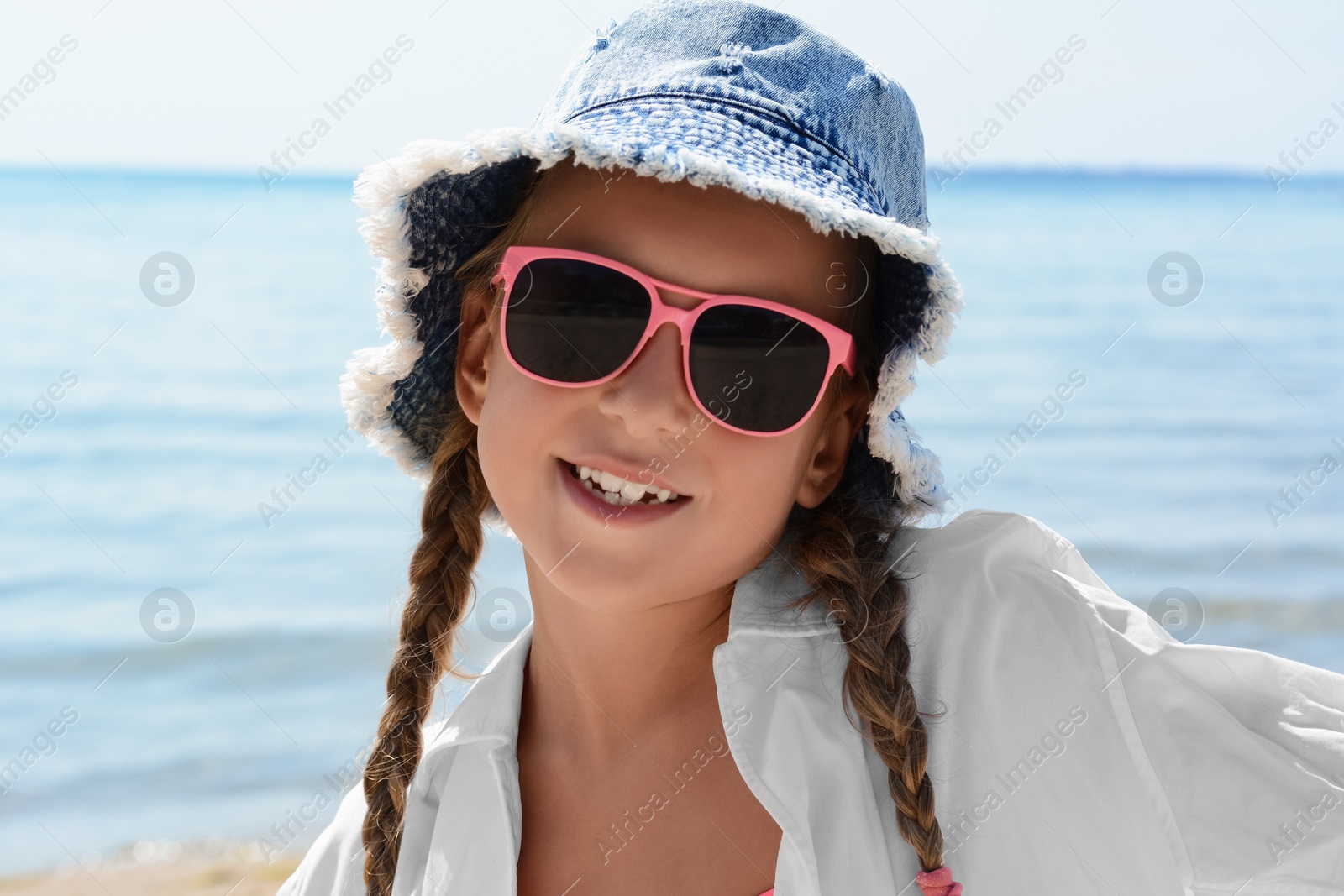 Photo of Little girl wearing sunglasses and hat at beach on sunny day