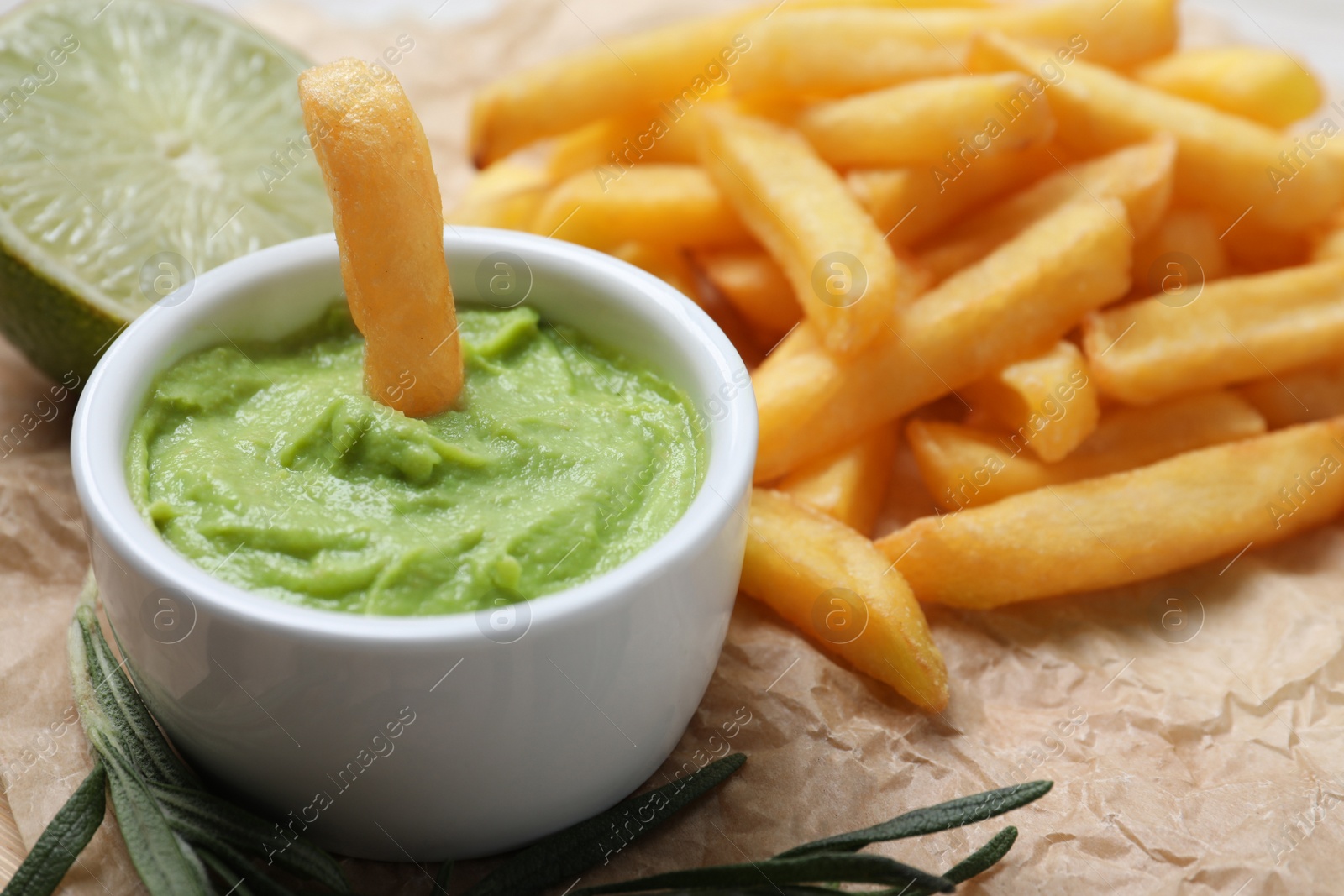 Photo of Delicious french fries, avocado dip, lime and rosemary on parchment