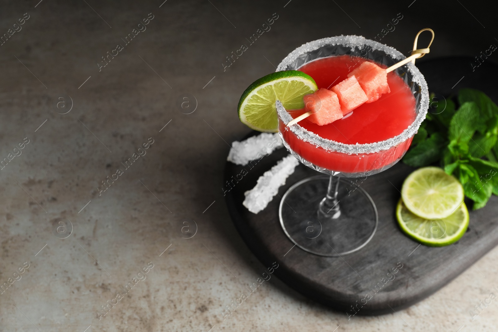 Photo of Cocktail glass of delicious fresh watermelon juice, lime and mint on grey table. Space for text