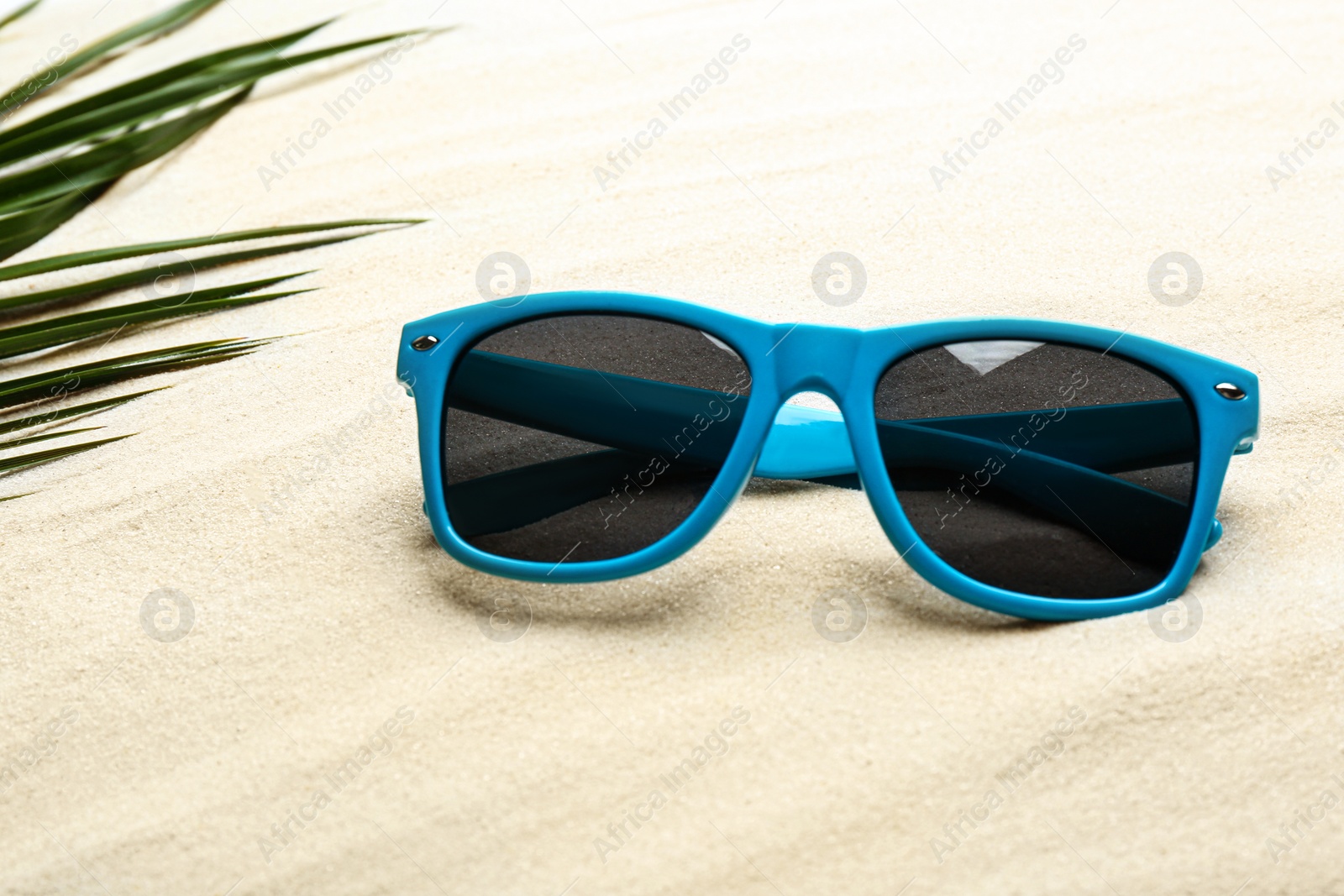 Photo of Stylish sunglasses and tropical leaf on white sand. Vacation time