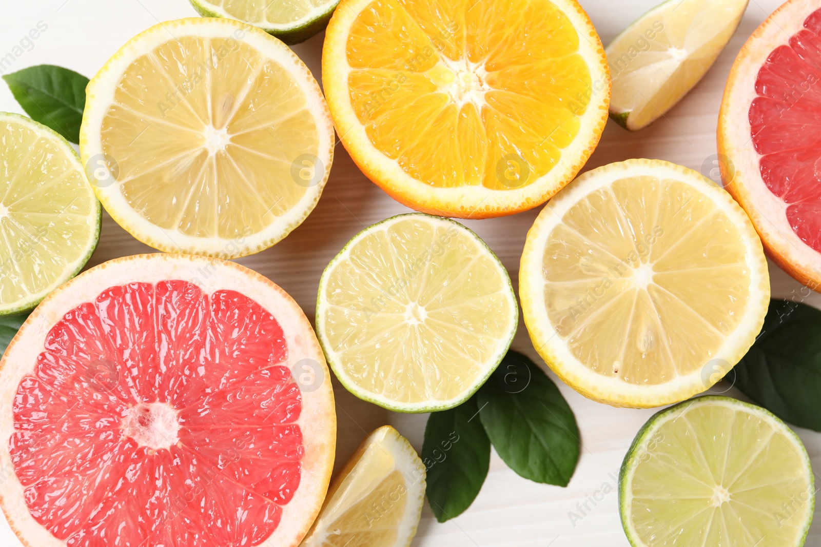 Photo of Different cut citrus fruits and leaves on white wooden table, flat lay