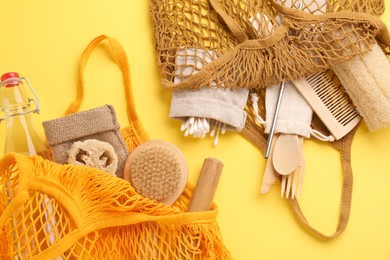 Photo of Fishnet bags with different items on yellow background, flat lay. Conscious consumption