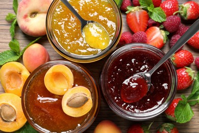 Photo of Jars with different jams and fresh fruits on wooden table, flat lay