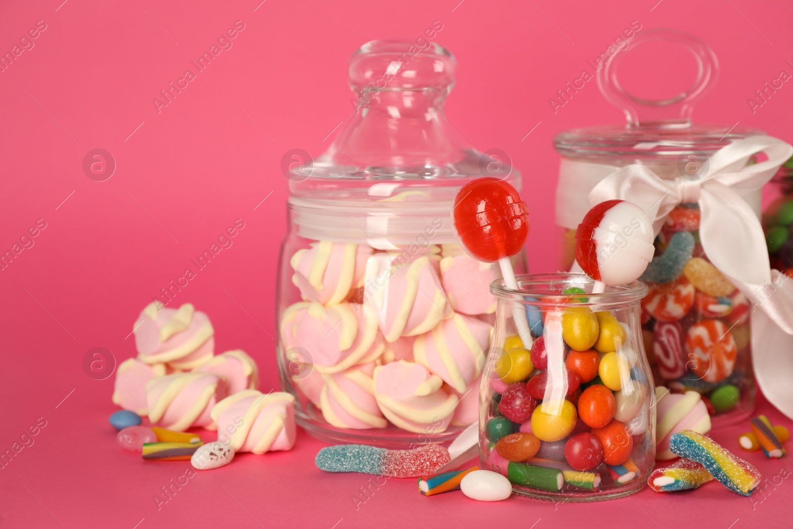 Photo of Glass jars with lots of different candies on bright pink background