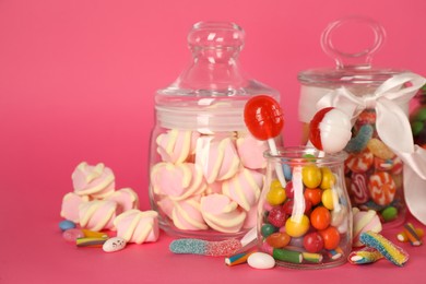 Glass jars with lots of different candies on bright pink background