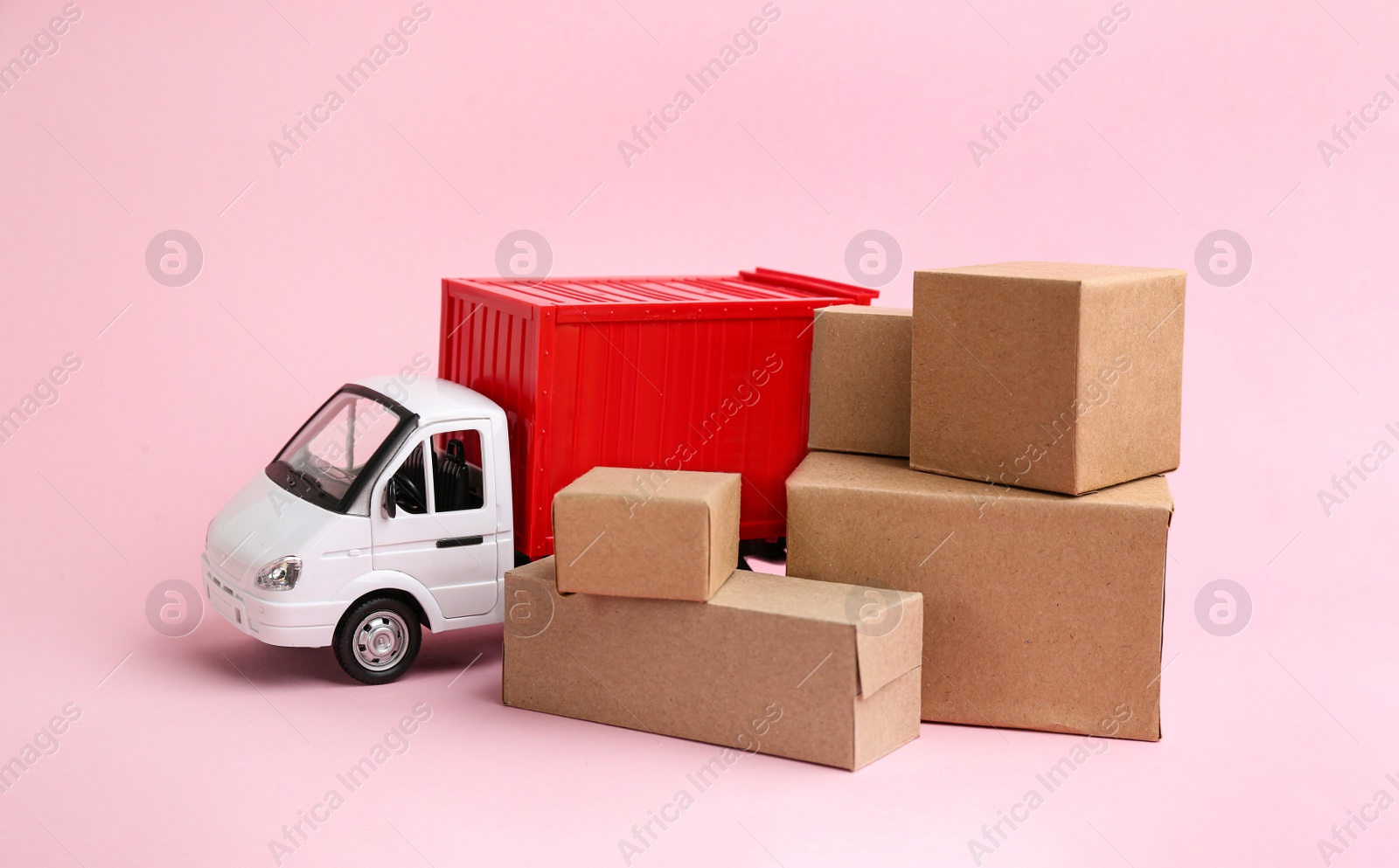 Photo of Truck model and carton boxes on light pink background. Courier service