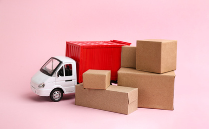 Photo of Truck model and carton boxes on light pink background. Courier service