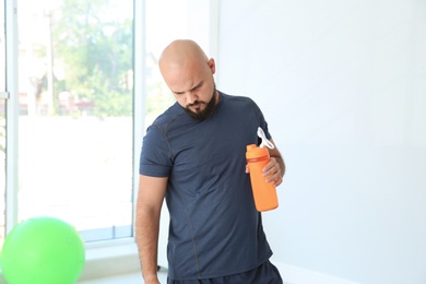 Tired overweight man with bottle of water in gym