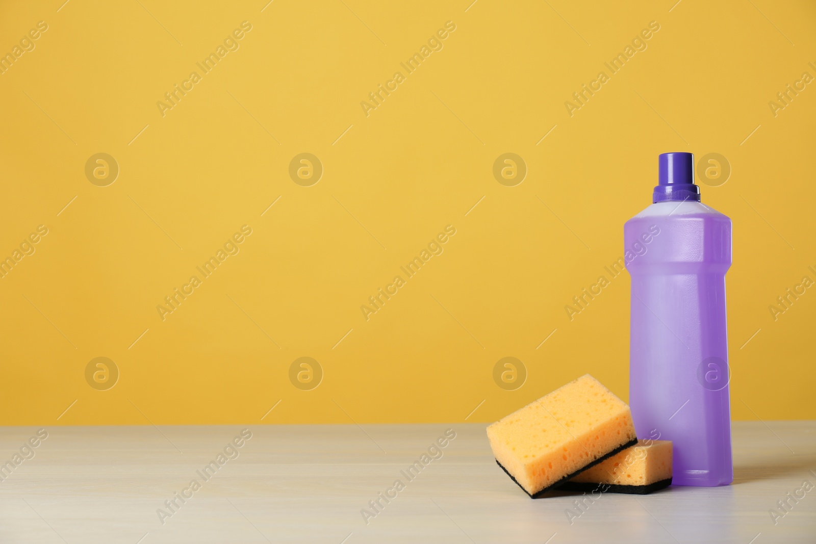 Photo of Bottle of cleaning product and sponges on light table. Space for text