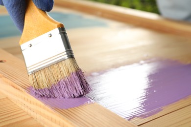 Worker applying violet paint onto wooden surface, closeup. Space for text