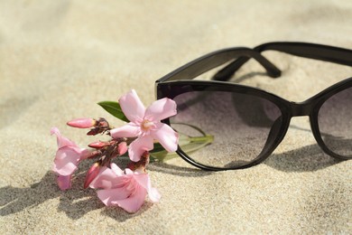 Photo of Beautiful sunglasses with flower on sand, closeup