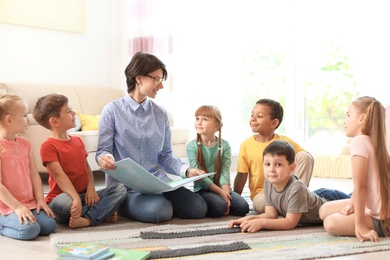 Photo of Young woman reading book to little children indoors. Learning by playing