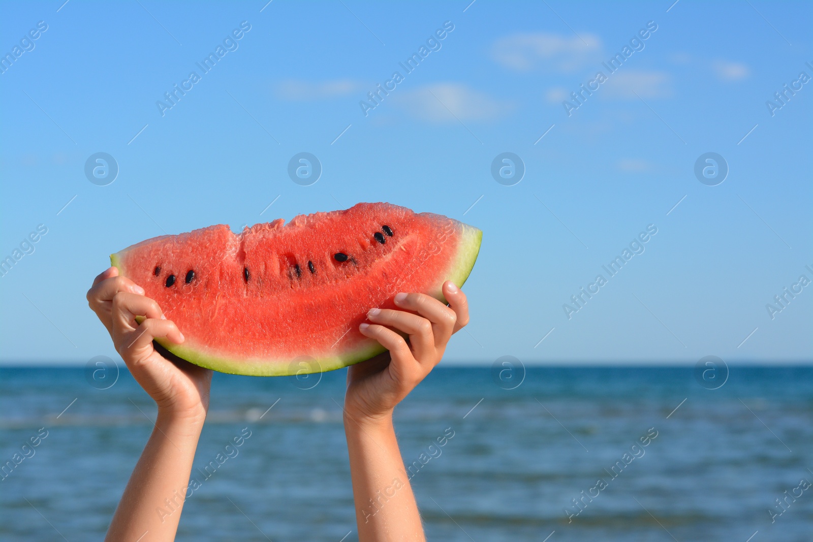 Photo of Child holding slice of fresh juicy watermelon near sea, closeup. Space for text