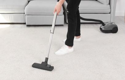 Photo of Young man removing dirt from carpet with vacuum cleaner at home