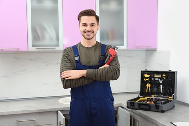 Photo of Male plumber with pipe wrench in kitchen. Repair service