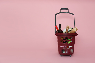Shopping basket full of different products on pink background. Space for text