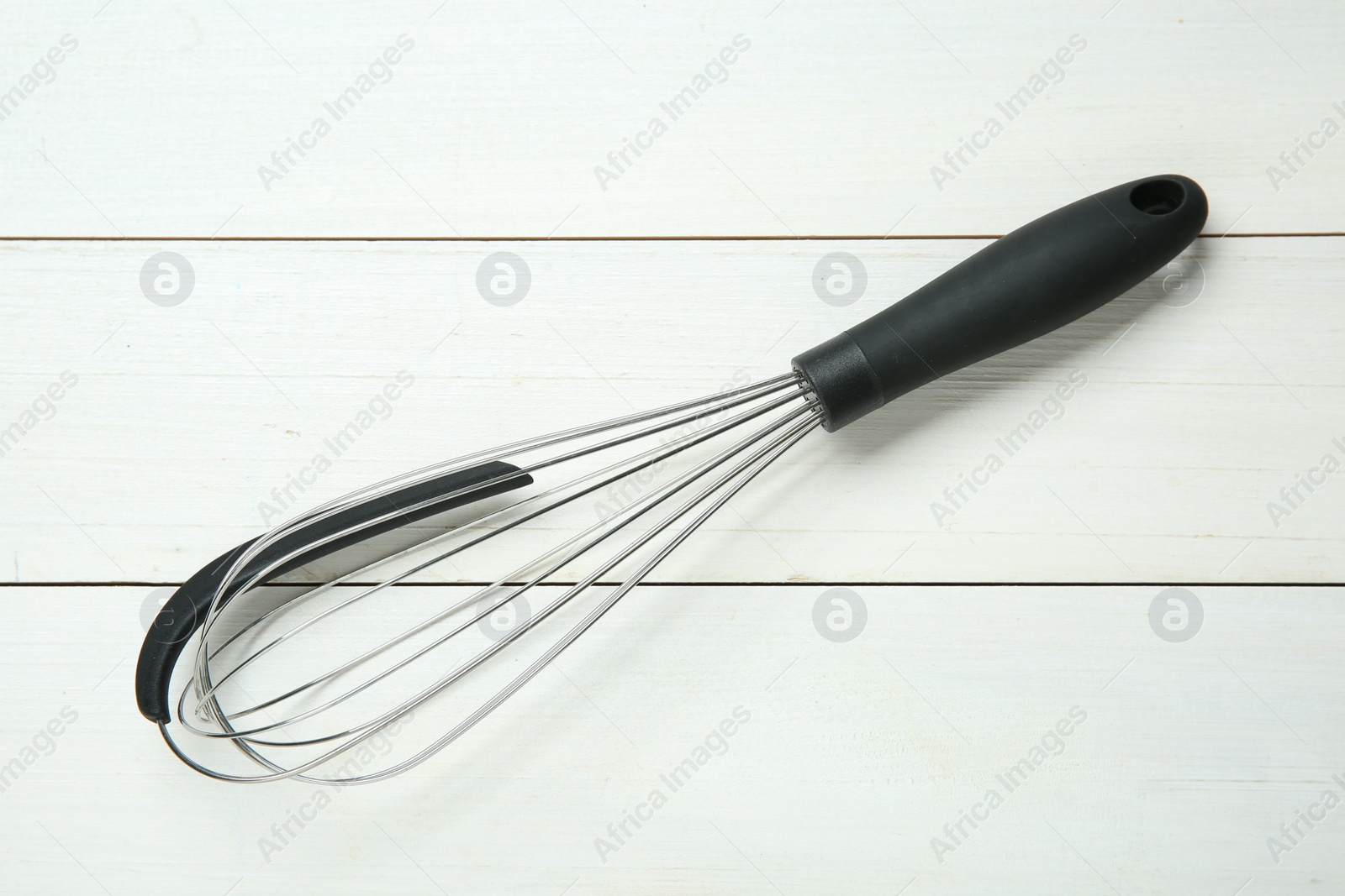 Photo of Metal whisk on white wooden table, top view