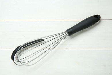 Metal whisk on white wooden table, top view