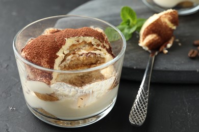 Photo of Delicious tiramisu in glass and spoon on black table, closeup