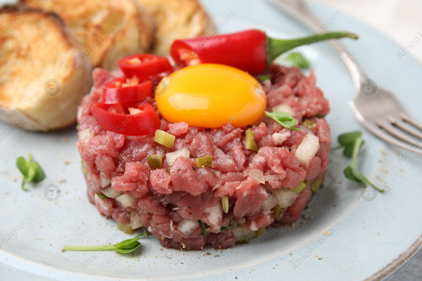 Photo of Tasty beef steak tartare served with yolk and other accompaniments on plate, closeup