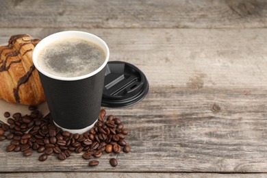 Coffee to go. Paper cup with tasty drink, croissant and beans on wooden table. Space for text