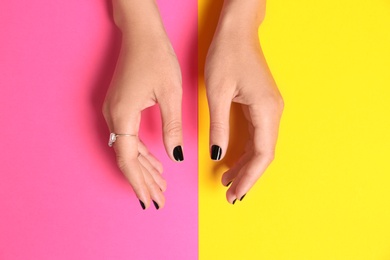 Woman showing manicure with black nail polish on color background, top view