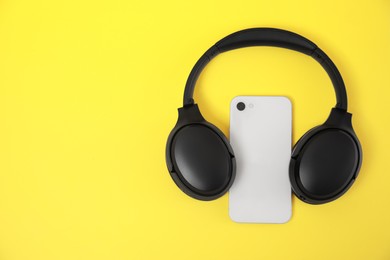 Photo of Modern wireless headphones and smartphone on yellow background, top view. Space for text