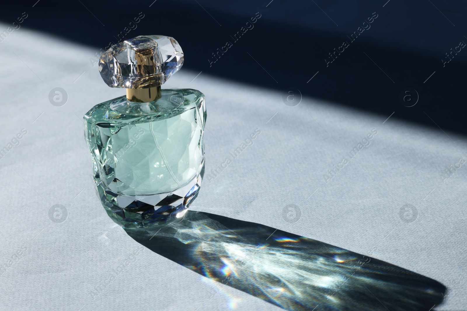 Photo of Luxury women's perfume. Sunlit glass bottle on grey background. Space for text
