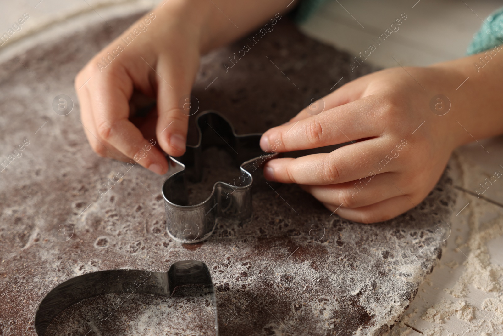 Photo of Little child cutting Christmas cookie at white wooden table, closeup