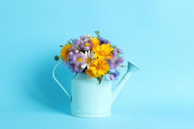 Watering can with beautiful flowers on light blue background