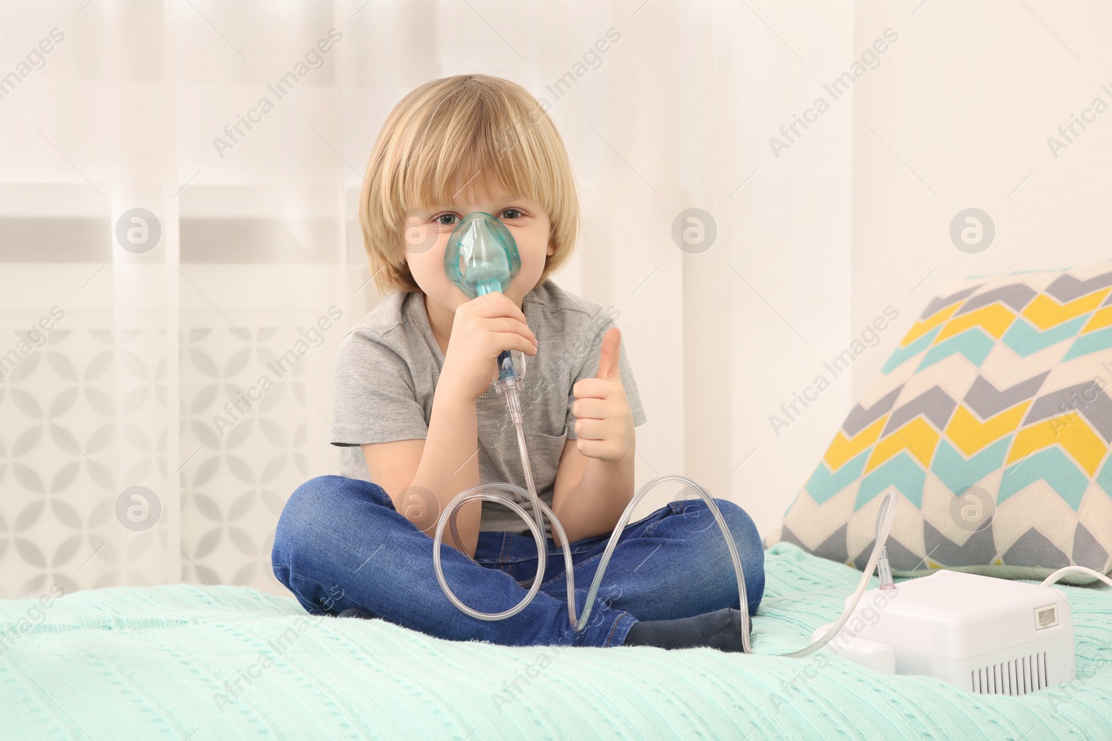 Photo of Sick little boy using nebulizer for inhalation on bed at home