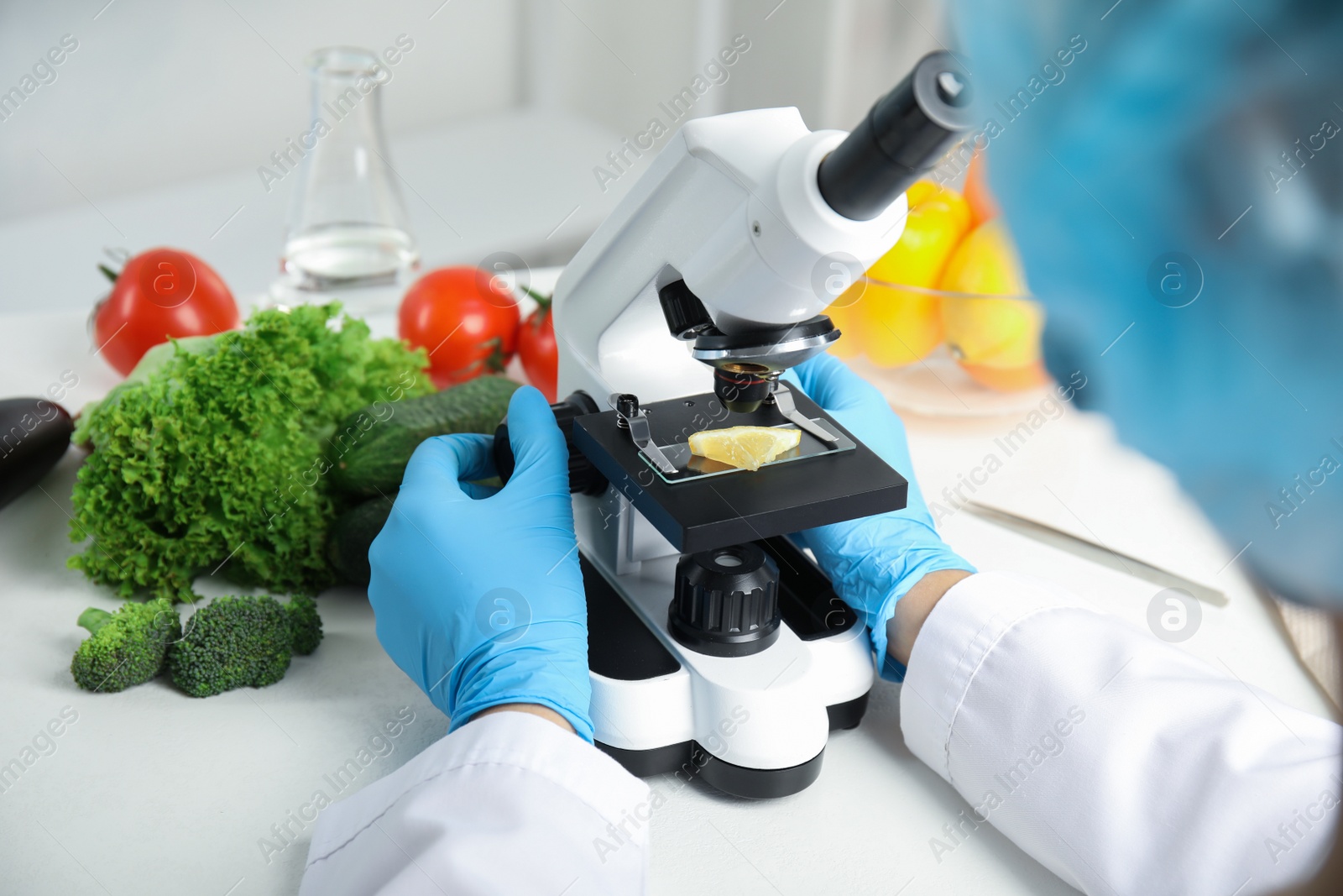 Photo of Scientist inspecting slice of lemon with microscope in laboratory, closeup. Poison detection