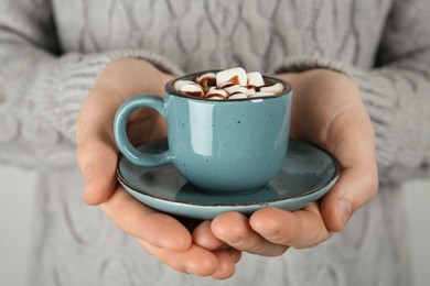 Photo of Woman holding cup of delicious hot chocolate with marshmallows and syrup, closeup