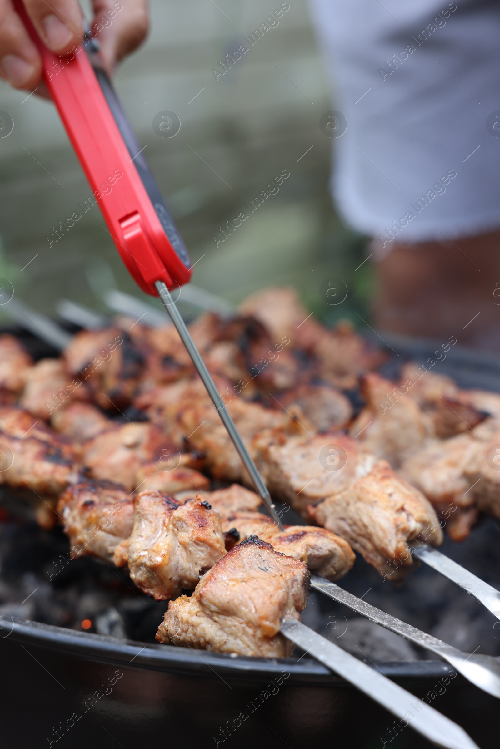 Photo of Man measuring temperature of delicious kebab on metal brazier outdoors, closeup