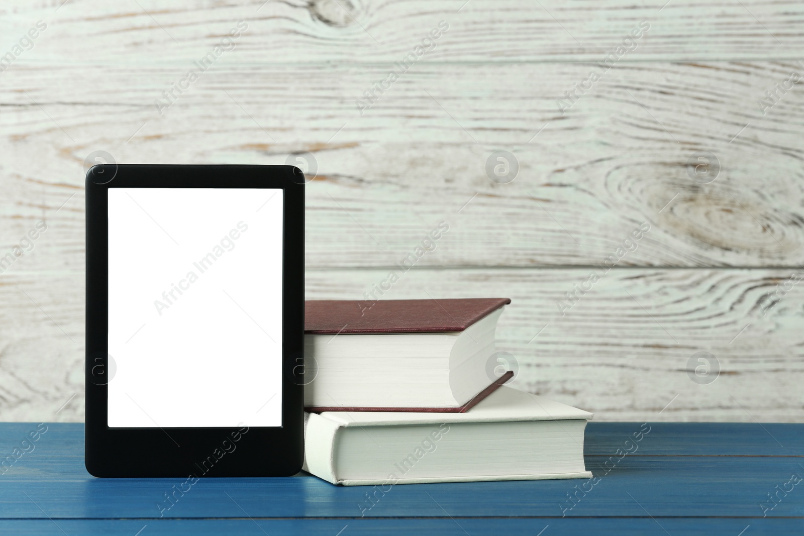 Photo of Portable e-book reader and hardcover books on blue wooden table, space for text