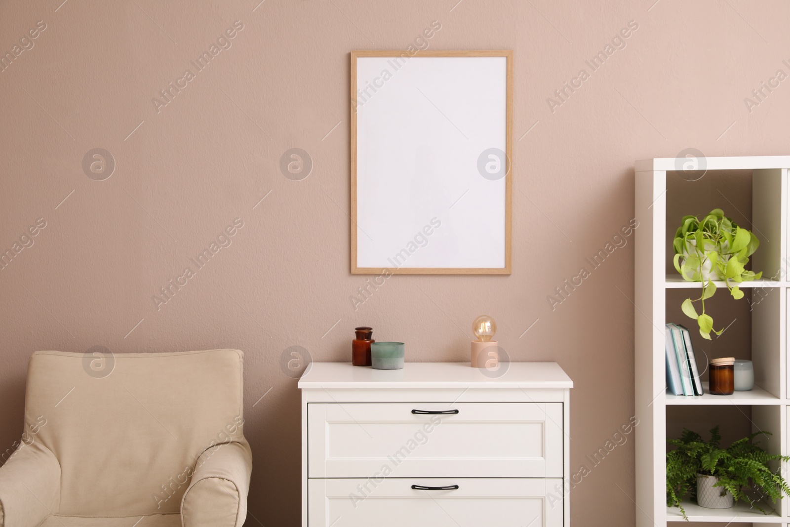 Photo of Empty frame hanging on pale rose wall over chest of drawers in living room. Mockup for design
