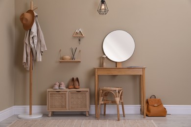 Photo of Modern hallway interior with stylish furniture, round mirror and wooden hanger for keys on beige wall